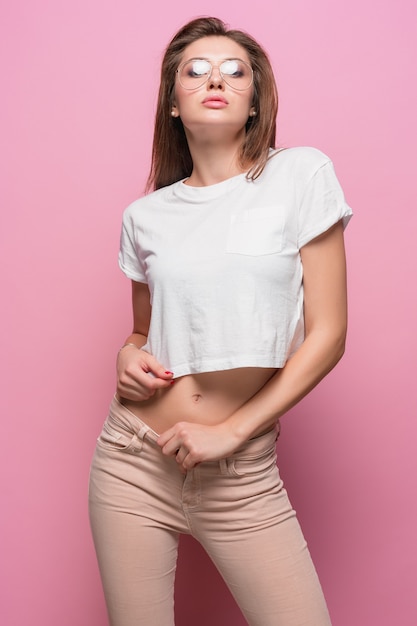 Jolie jeune femme sensuelle de la mode sexy posant sur fond rose vêtue d'un jean de style hipster