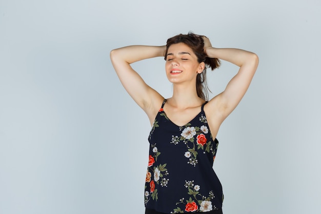 Jolie jeune femme serrant la tête avec les mains en blouse et l'air détendue. vue de face.