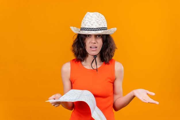 Photo gratuite une jolie jeune femme surprenante aux cheveux courts dans une chemise orange portant un chapeau de soleil tenant une carte