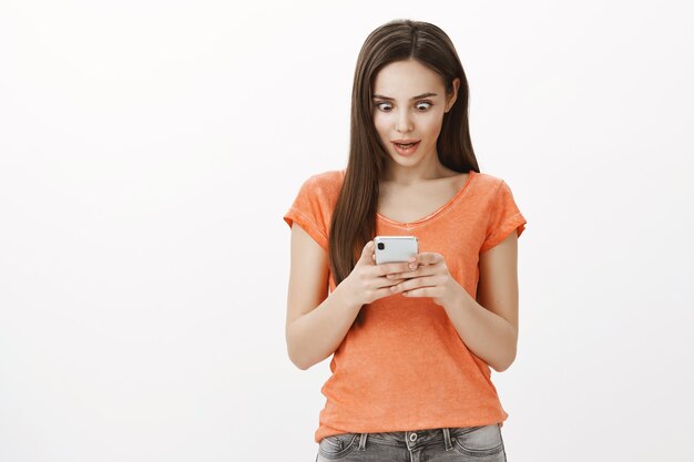 Jolie jeune femme surprise et étonnée à l'aide de téléphone mobile