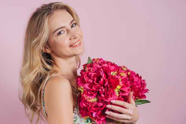 Une jolie jeune femme tenant de belles fleurs rouges sur fond rose