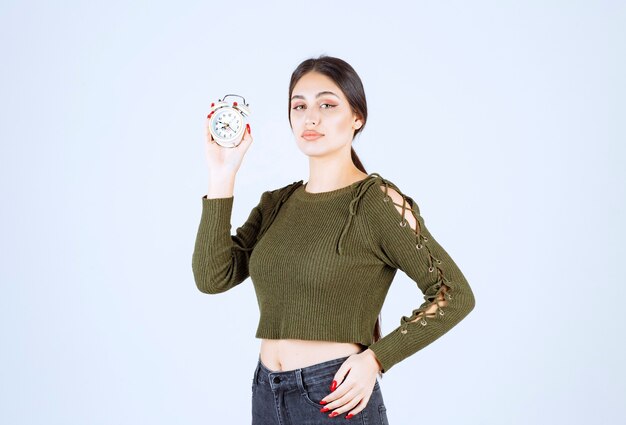 Jolie jeune femme tenant un réveil sur fond blanc.