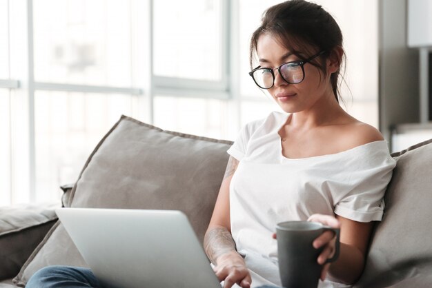 Jolie jeune femme tenant une tasse de café à l'aide d'un ordinateur portable.