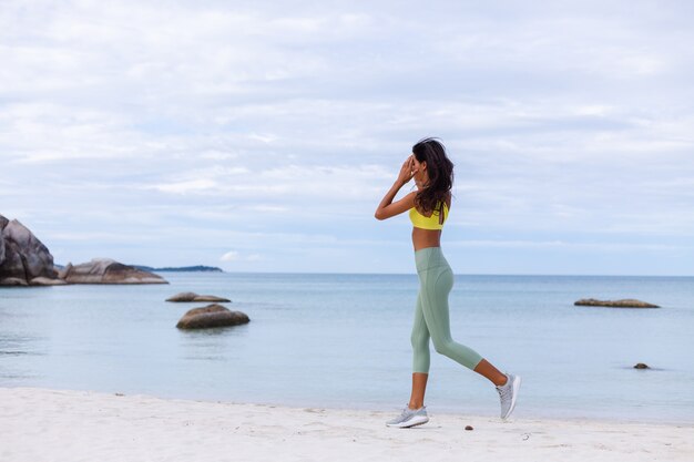 Jolie jeune femme en vêtements de sport colorés sur la plage