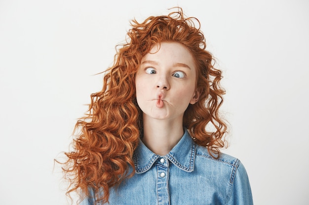 Jolie jeune fille aux cheveux bouclés foxy faisant la grimace. Copiez l'espace.