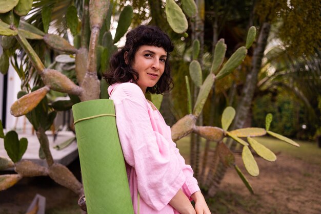 Jolie jeune fille brune caucasienne porter une chemise détient un tapis de yoga dans un jardin tropical concept de plaisir de week-end d'été