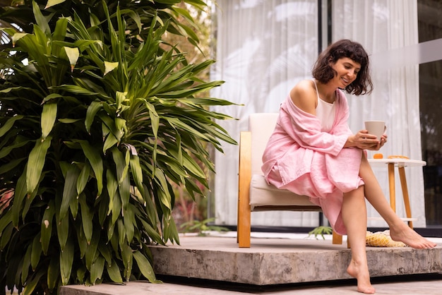 Jolie jeune fille européenne aux cheveux noirs tient une tasse de thé tout en étant assis sur la terrasse d'été Bonjour concept