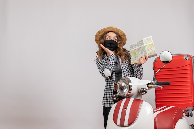 jolie jeune fille avec un masque tenant une carte debout près d'un cyclomoteur