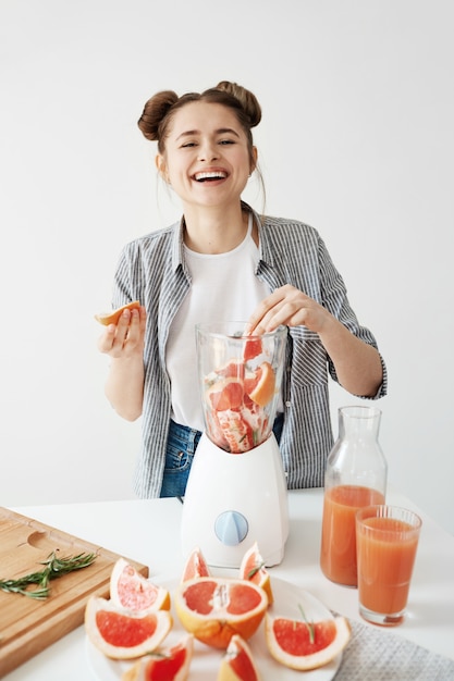 Jolie jeune fille souriante mélange smoothie détox rafraîchissant pamplemousse sur mur blanc. Concept d'aliments sains.