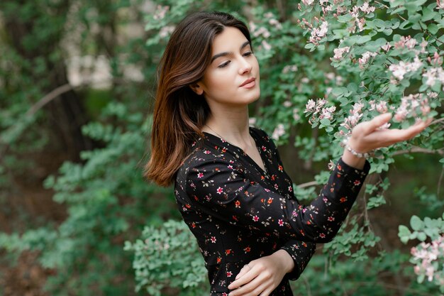 Jolie jeune mannequin ayant une séance photo dans un jardin fleuri touchant la fleur en admirant