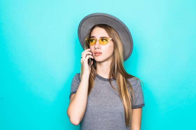 Jolie jeune mannequin en t-shirt, chapeau et lunettes transparentes parle au téléphone isolé sur fond vert