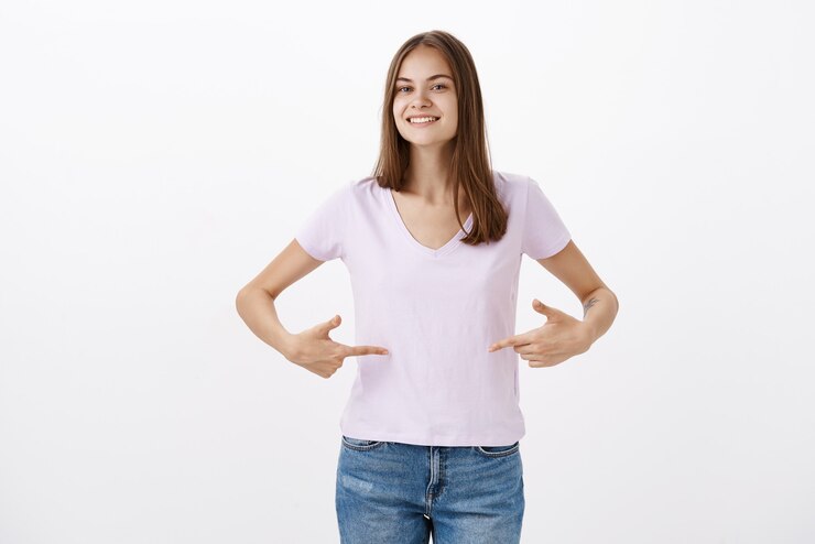Photo gratuit jolie jeune sportive donnant des conseils sur la façon de rester en forme en souriant joyeusement en regardant amicalement pointant sur le t-shirt ou le ventre debout ravi et heureux avec un regard heureux sur un mur gris