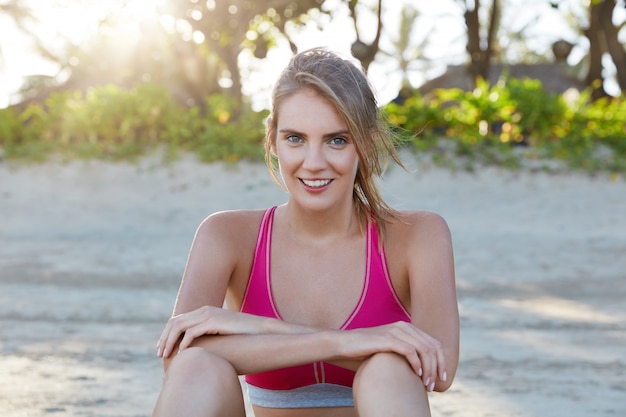 Jolie joggeuse heureuse étant motivée, s'entraîne le matin sur la plage de sable, se repose seule, porte un haut rose. Sportive impliquée dans un mode de vie actif. Personnes, fitness et exercices en plein air