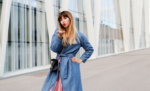 Jolie jolie femme en manteau bleu posant sur des bâtiments modernes