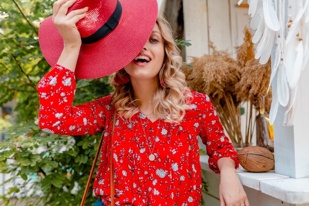 Jolie jolie femme souriante blonde élégante en chapeau rouge paille et chemisier tenue de mode d'été café