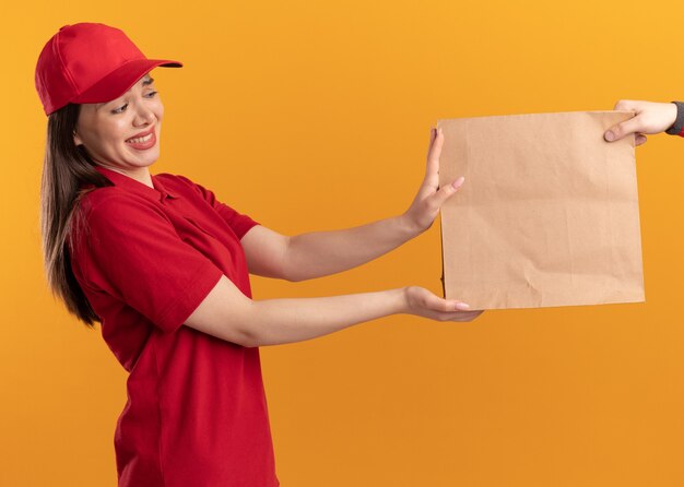 Une jolie livreuse inquiète en uniforme donne un paquet de papier à quelqu'un