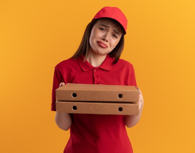 Une jolie livreuse mécontente en uniforme tient des boîtes à pizza
