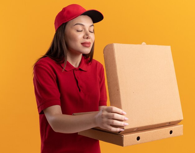 Une jolie livreuse ravie en uniforme tient des boîtes à pizza et fait semblant de renifler