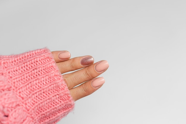 Jolie manucure de couleur nude, un doigt doré brillant, sur fond de coussin en laine rose tricoté