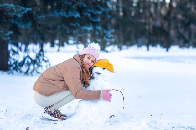 Jolie petite adolescente s'amusant à faire un bonhomme de neige dans la forêt d'hiver enneigée
