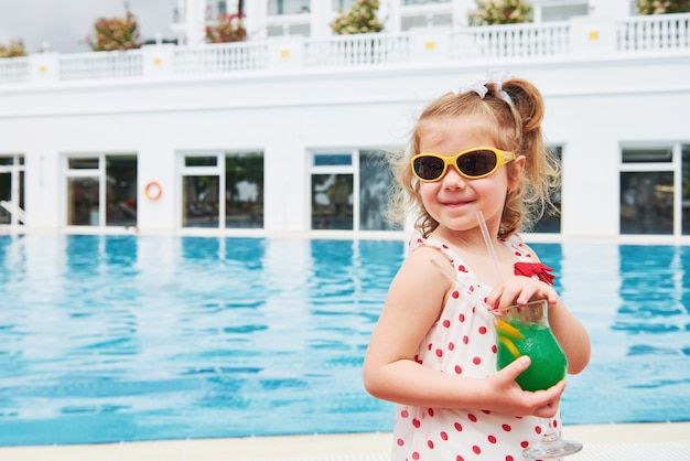 Jolie petite blonde à la piscine et tenant le cocktail d'un enfant.