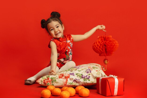 Jolie petite fille asiatique tenant une lanterne isolée sur un mur rouge en vêtements traditionnels