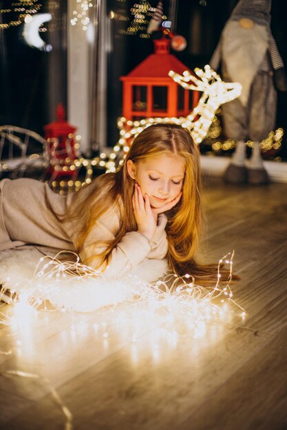 Jolie petite fille assise près des lumières de Noël à la veille