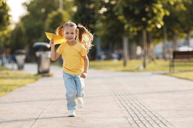 jolie petite fille avec un avion en papier en plein air