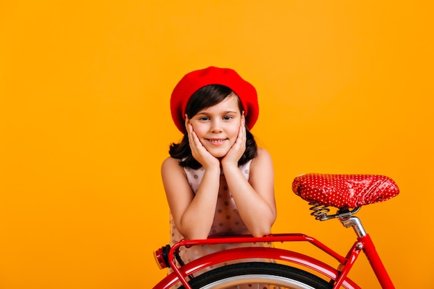Jolie petite fille en béret français posant avec vélo. enfant souriant isolé sur jaune.