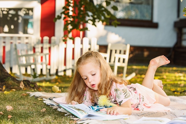 Jolie petite fille blonde livre de lecture à l'extérieur sur l'herbe