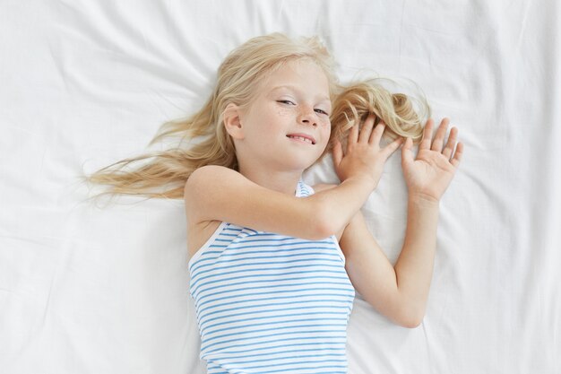 Jolie petite fille blonde qui s'étend dans un lit blanc