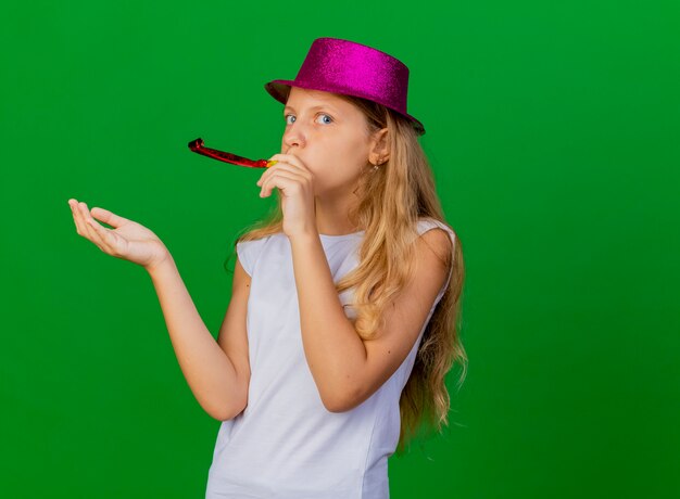 Jolie petite fille en chapeau de vacances soufflant sifflet pour célébrer l'anniversaire