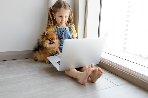 jolie petite fille avec un chien et un ordinateur portable à la maison