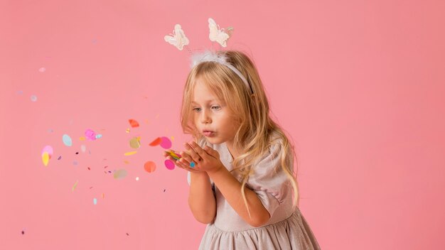 Jolie petite fille en costume soufflant des confettis