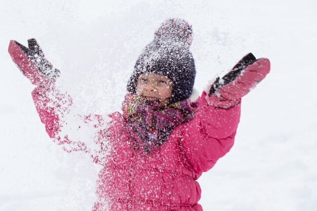 Une jolie petite fille dans une veste rose et un chapeau joue dans la neige. Concept de divertissement pour enfants d'hiver.