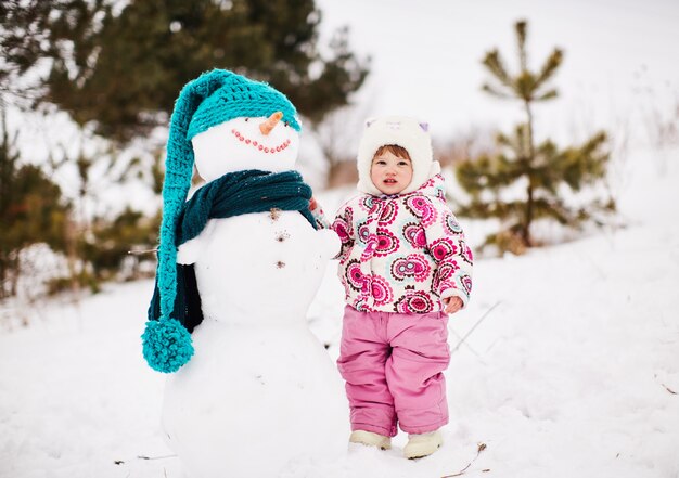 Une jolie petite fille est debout près d&#39;un bonhomme de neige souriant