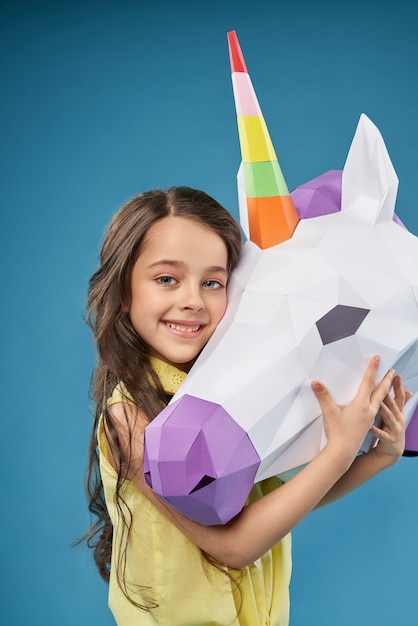 Jolie petite fille étreignant la tête de licorne 3D blanche.