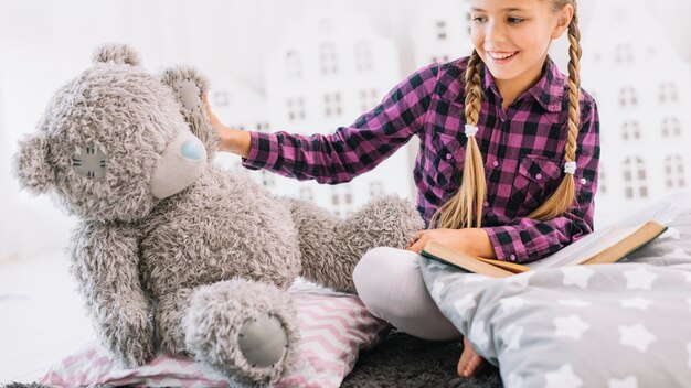 Jolie petite fille lisant un livre avec son ours en peluche