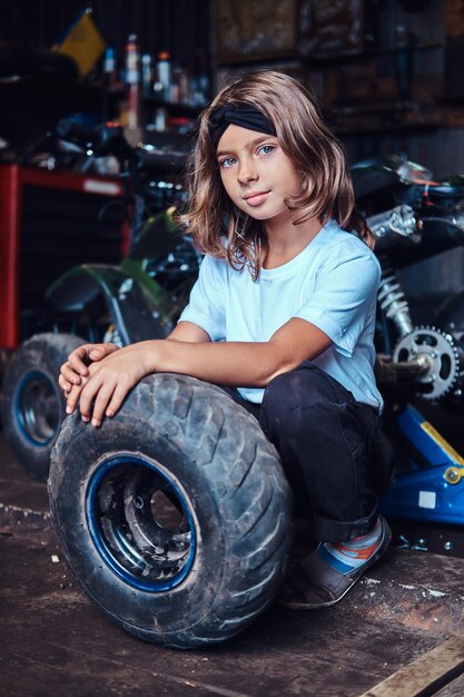 Une jolie petite fille pose pour un photographe avec une grande roue de voiture au service automobile.