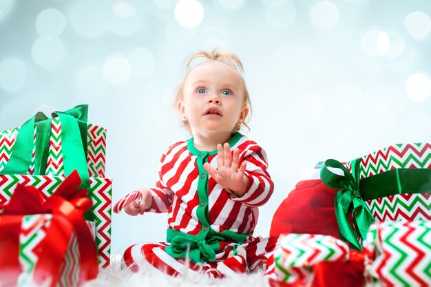 Jolie petite fille près du bonnet de Noel posant sur fond de Noël avec décoration. Assis sur le sol avec boule de Noël.