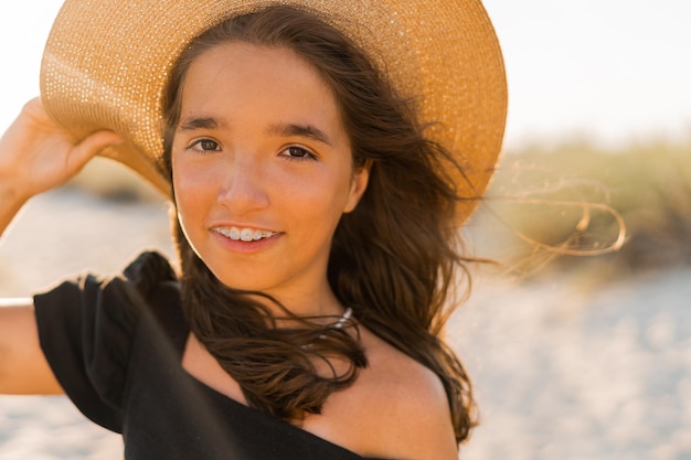 Photo gratuite jolie petite fille en robe de lin élégante et chapeau de paille posant sur la plage couleurs chaudes du coucher du soleil