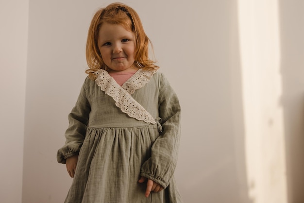 Jolie petite fille rousse à la peau claire dans des vêtements décontractés regarde la caméra sur fond blanc Concept de bébé fille