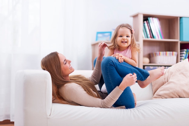 Jolie petite fille s'amuser avec la mère sur le canapé