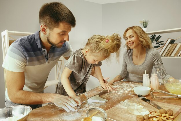 Jolie petite fille et ses beaux parents préparent la pâte pour le gâteau dans la cuisine à la maison.