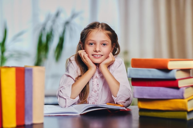 Jolie petite fille à la table avec beaucoup de livres colorés.