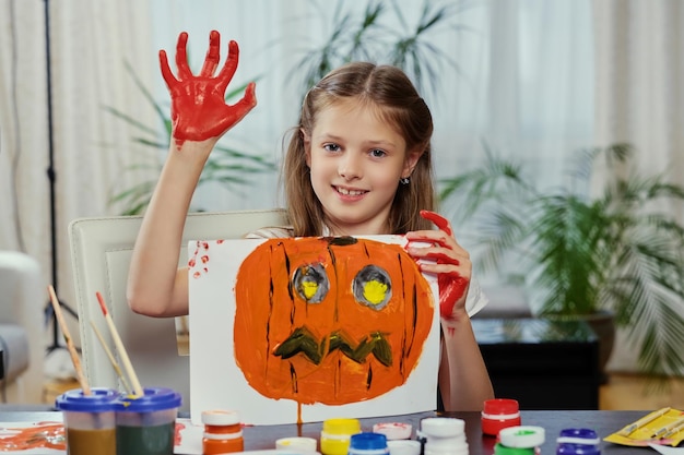 La jolie petite fille tient une affiche avec une citrouille d'Halloween peinte.