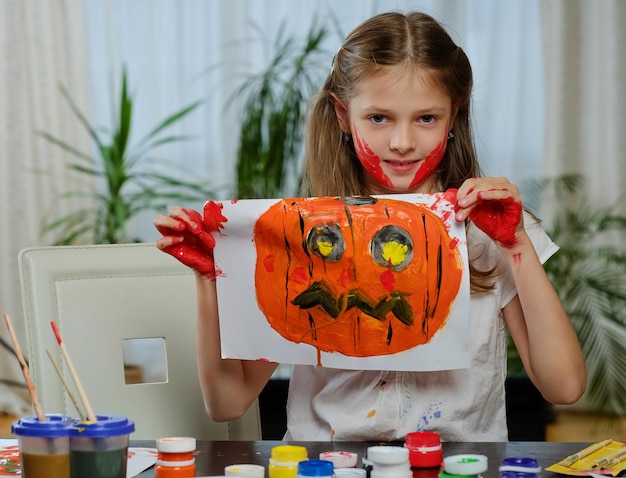 La jolie petite fille tient une affiche avec une citrouille d'Halloween peinte.