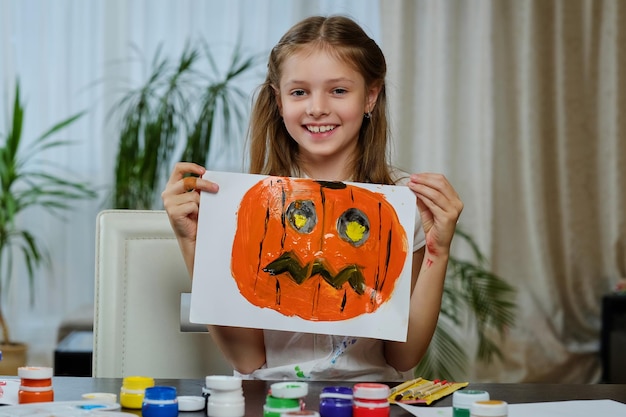 La jolie petite fille tient une affiche avec une citrouille d'Halloween peinte.