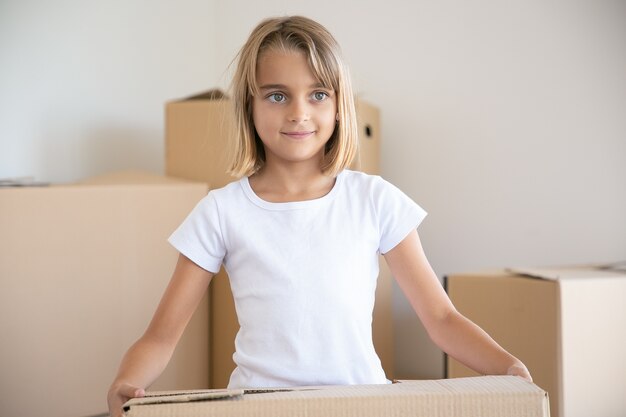 Jolie petite fille transportant une boîte en carton et regardant ailleurs