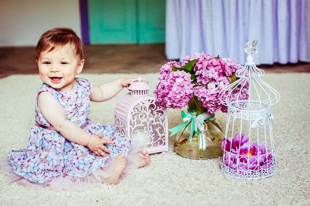 Une jolie petite fille vêtue de fleurs se trouve devant la lanterne rose et le bouquet de lilas